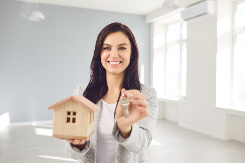 Jeune agente immobilière brune tenant une miniature de maison en bois et des clés