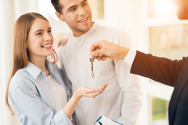 Agent immobilier sans diplôme, tendant les clés d’un bien au jeune couple qui vient de l’acheter
