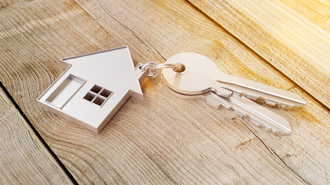 Gros plan sur des clés avec un porte-clé en métal représentant une maison, sur un support en bois